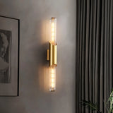 "A modern brass wall sconce with a vertical glass tube illuminating a room with soft light."
