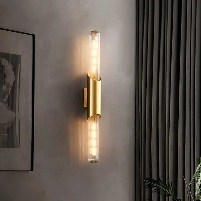 "A modern brass wall sconce with a vertical glass tube illuminating a room with soft light."