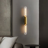 "A modern brass wall lamp with a vertical glass tube on a gray wall."