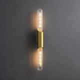 "A modern brass wall lamp with a vertical ribbed glass tube on a dark gray wall."
