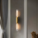 "A modern brass wall sconce with a vertical glass tube mounted on a textured wall."