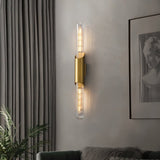 "A modern brass wall lamp with a vertical glass tube illuminating a living room."