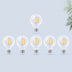Six LED filament bulbs with warm golden filaments arranged in two rows against a light blue background with plant foliage.