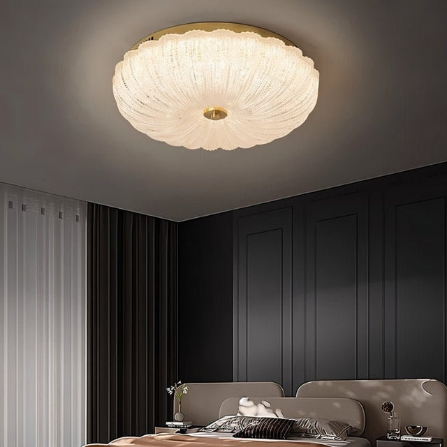 "A modern glass ceiling light with a brass frame, mounted on a ceiling in a contemporary bedroom."