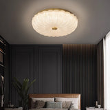 "A modern glass ceiling light with a brass frame, illuminating a contemporary bedroom with a dark accent wall."