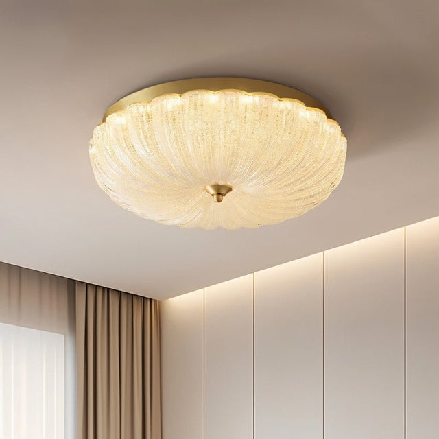 "A modern ceiling light with a brass frame and glass shade, mounted on a white ceiling."