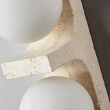 "Close-up of a modern travertine wall lamp with two spherical white glass shades, showcasing the texture of the natural stone."