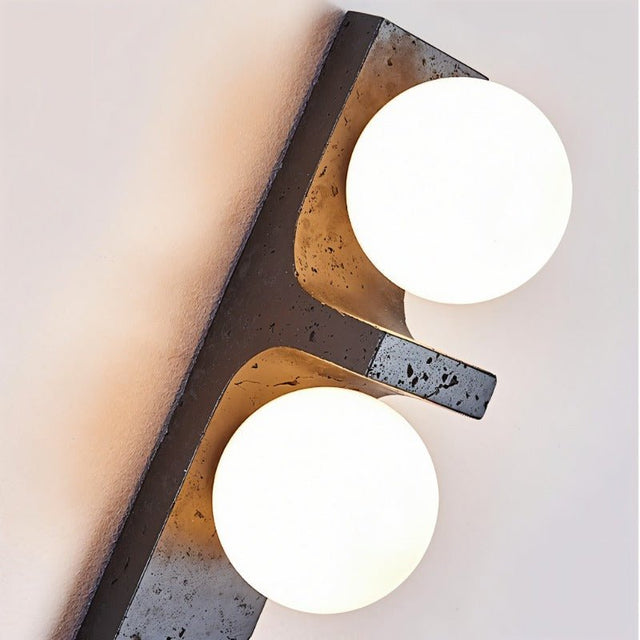"Close-up of a modern travertine wall lamp with two spherical white glass shades, showcasing the texture of the natural stone and the soft glow of the light."