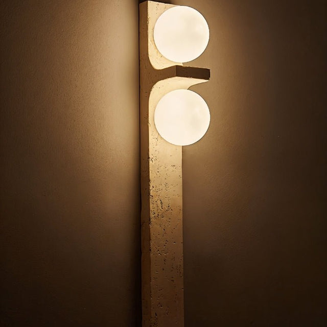 "Modern wall lighting fixture with two frosted glass globes mounted on a vertical travertine base, casting a warm, ambient glow."