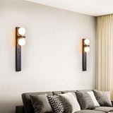 "Two modern travertine wall lamps with two frosted glass globes each, mounted on a wall on either side of a sofa in a living room."
