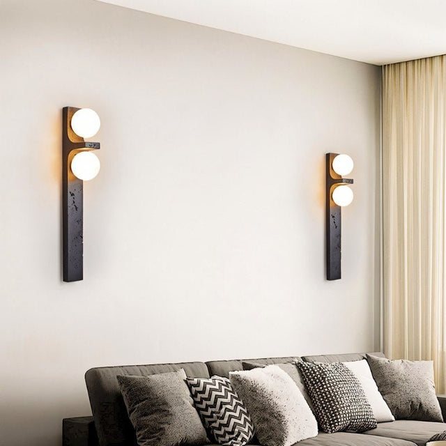 "Two modern travertine wall lamps with two frosted glass globes each, mounted on a wall on either side of a sofa in a living room."