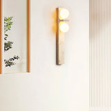 "A modern travertine wall sconce with two spherical white glass shades mounted on a vertical travertine base."