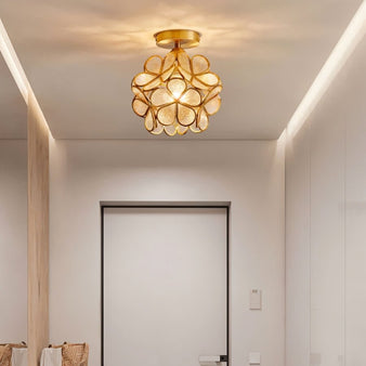 "A floral-inspired ceiling light with a brass frame and luminous glass petals, illuminating a modern entryway with white walls and a dark door."