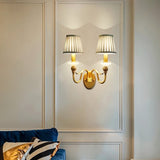 "A double-arm brass wall lamp with jade accents and fabric shades, illuminating a living room with a blue sofa."