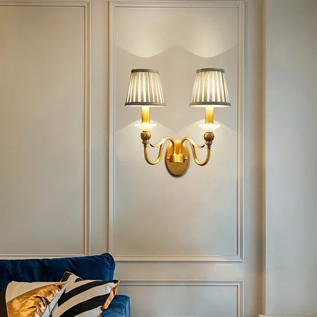 "A double-arm brass wall lamp with jade accents and fabric shades, illuminating a living room with a blue sofa."