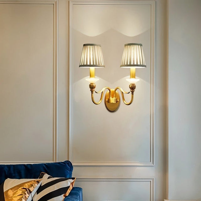 "A double-arm brass wall lamp with jade accents and fabric shades, illuminating a living room with a blue sofa."