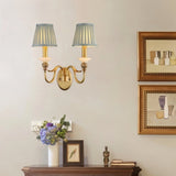 "A double-arm brass wall lamp with jade accents and fabric shades, mounted on a wall above a wooden console table."