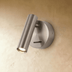Black cylindrical wall-mounted reading light on white bedroom wall above wooden nightstand with flowers and picture frame.