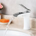 Chrome waterfall bathroom faucet with white ceramic base flowing water over sink counter.