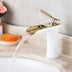 White ceramic bathroom sink faucet with gold-tone brass spout and handle, water flowing, displayed on marble countertop.