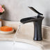 Black waterfall bathroom faucet with curved spout running water over a light marble sink.
