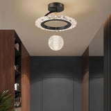 "A black ceiling light with a circular frame and a hanging crystal sphere, installed in a hallway with a dark gray door and dark wood paneling."