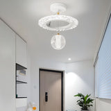 "A white ceiling light with a circular frame and a hanging crystal sphere, installed in a hallway with a dark door and a potted plant."