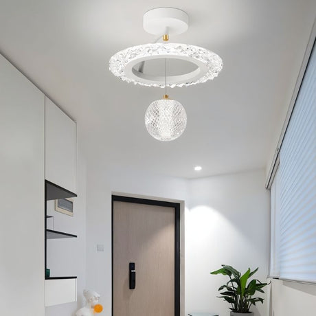 "A white ceiling light with a circular frame and a hanging crystal sphere, installed in a hallway with a dark door and a potted plant."