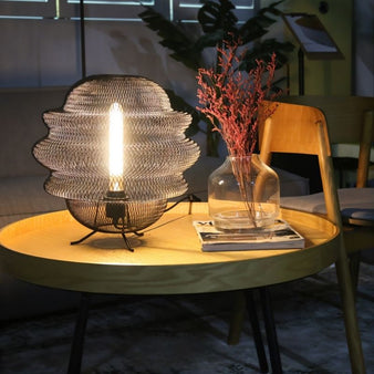 "Black metal mesh table lamp lit on a round table in a living room,"Supply