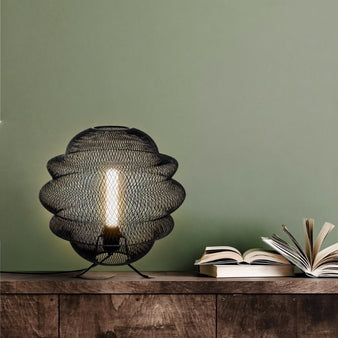 "Black metal mesh table lamp on a wooden table with open books,"