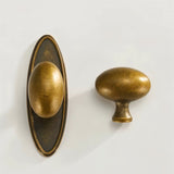 "Pair of oval antique brass knobs, one with a backplate, showcasing their smooth, ergonomic design for cabinets and drawers."