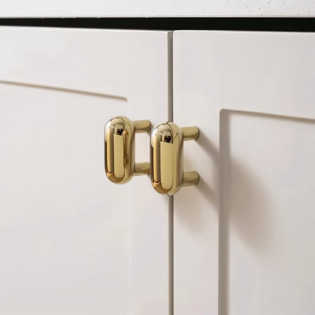 "Pair of sleek, capsule-shaped brass knobs on modern white cabinets."