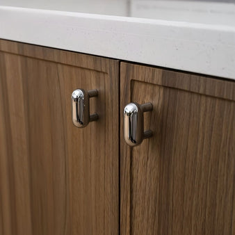 "Pair of sleek, capsule-shaped chrome knobs on a modern wooden bathroom vanity with a white countertop."