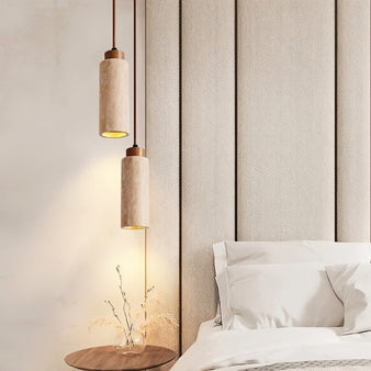 "Pair of modern minimalist pendant lights with travertine bodies in cylindrical and rectangular shapes, hanging above a bedside table in a contemporary bedroom."