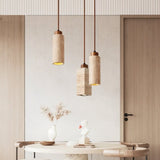 "Trio of modern minimalist pendant lights with travertine bodies in cylindrical and rectangular shapes, creating a balanced asymmetry above a contemporary dining table."