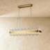 Round brass chandelier with crystal glass panels, suspended above cream sectional sofa in modern bedroom setting.