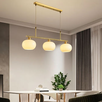 "A 3-light linear chandelier with opal glass globes and a gold metal frame, hanging above a dining table in a modern dining room."