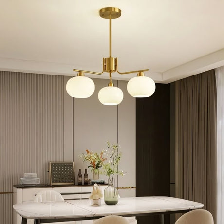 "A 3-light round chandelier with opal glass globes and a gold metal frame, hanging above a dining table in a modern dining room."