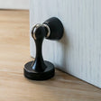 "A sleek, black magnetic door stop made of zinc-alloy with a contoured design, installed on a door to prevent slams and wall damage in a modern interior."