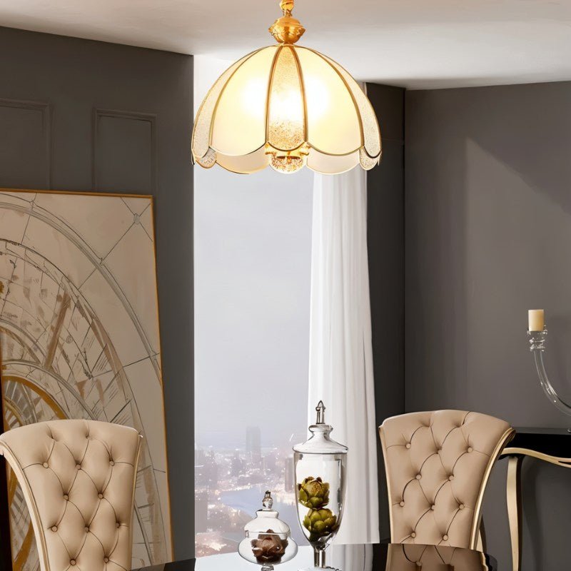 "A vintage-style pendant light with a scalloped glass shade and copper frame hanging above a dining table with chairs."