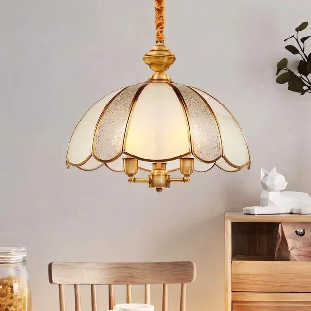 "A vintage-style pendant light with a scalloped glass shade and copper frame hanging above a dining table with a chair."