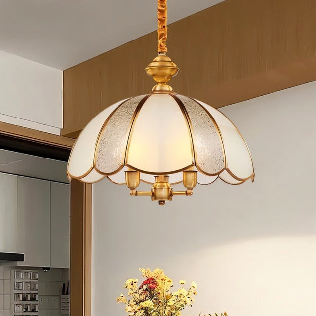 "A vintage-style pendant light with a scalloped glass shade and copper frame hanging in a room above a table."