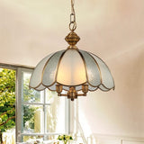 "A vintage-style pendant light with a scalloped glass shade and copper frame hanging above a table in a bright room."