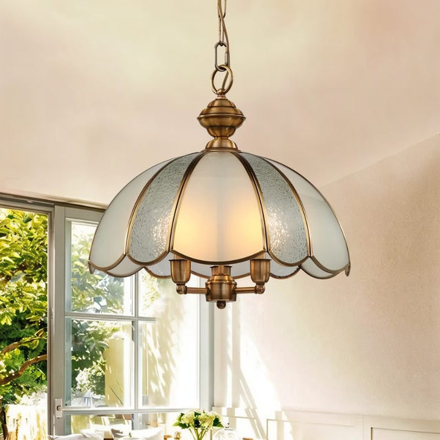 "A vintage-style pendant light with a scalloped glass shade and copper frame hanging above a table in a bright room."