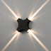 Black modern wall lamp with four directional light beams against gray wall.