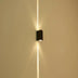 Black rectangular wall lamp mounted on beige wall, emitting upward and downward light beams.