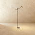 Minimalist floor lamp with brass head and gray pole on white base, studio setting, three-quarter view.