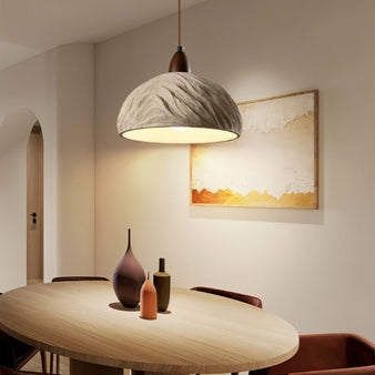 "Wabi Sabi cement pendant light with a minimalist shape and industrial finish, hanging over a round dining table in a contemporary dining room."