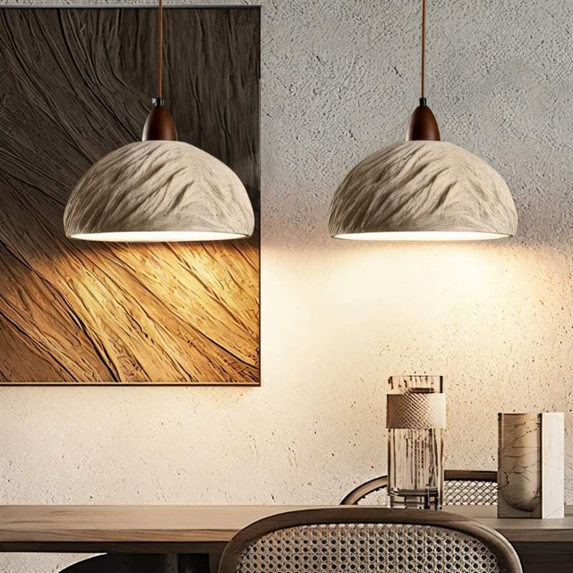 "Pair of Wabi Sabi cement pendant lights with raw textures, hanging over a dining table in a contemporary dining room with artwork on the wall."