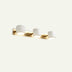 Three-light wall sconce with brass bar and white cylindrical shades against a neutral beige background.